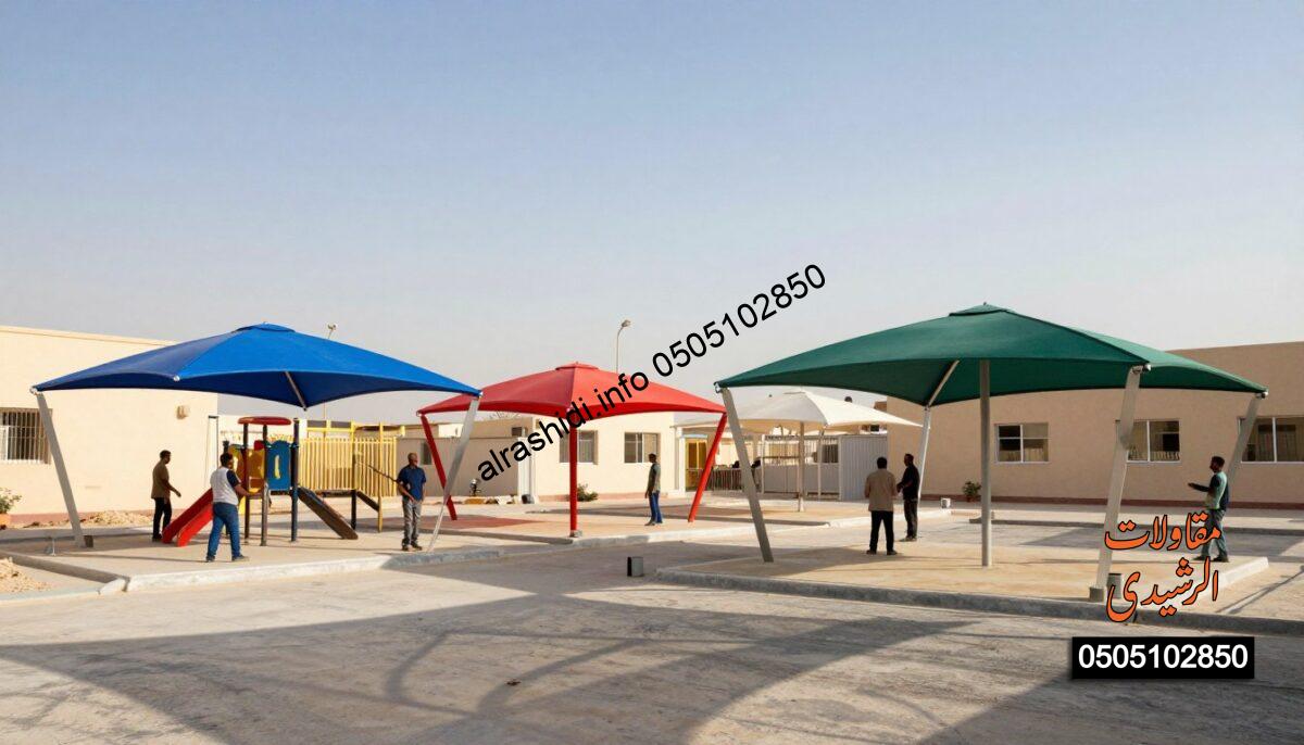 A realistic construction scene depicting various types of school shade structures in a schoolyard setting in West Riyadh. In the foreground, workers in professional attire are installing large, colorful, fabric and metal shades over playground areas and parking spaces. In the middle ground, several distinct styles of shades are visible: a modern, angular structure in vibrant blue, a classic dome-shaped shade in bright red, and a wide, traditional canopy in green. The background shows a sunny day with a clear blue sky, adding a warm and inviting atmosphere. Soft shadows from the shades create interesting patterns on the ground. The scene captures a sense of community and progress, emphasizing quality craftsmanship in these installations.