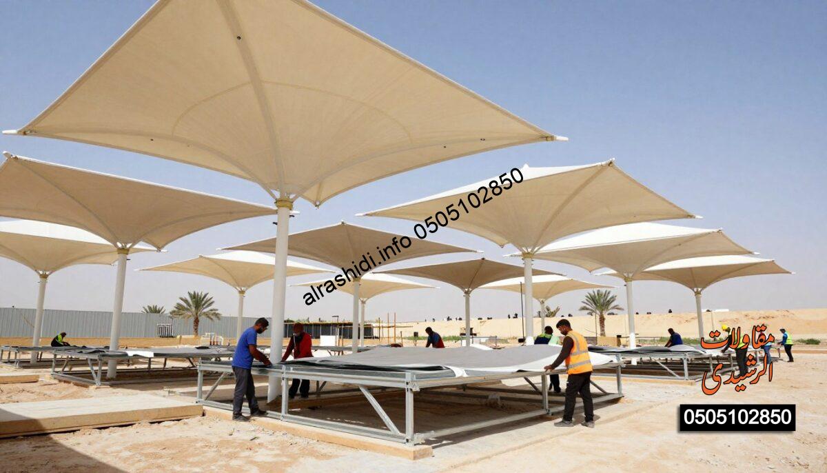 A realistic construction scene showcasing structural tension canopies, known as "مظلات الشد الإنشائي", being installed in a sunny outdoor environment. In the foreground, skilled workers in professional attire are meticulously assembling metal frames and fabric covers, demonstrating teamwork and precision. The middle ground features various shades in different stages of installation, displaying their modern design and functionality. In the background, the Saudi Arabian landscape is visible, with clear blue skies and a few palm trees swaying gently. The lighting is bright and natural, highlighting the textures of the materials used. A slight low-angle perspective enhances the dramatic appearance of the canopies, emphasizing their architectural elegance. The overall atmosphere is dynamic and industrious, reflecting the craftsmanship involved in creating durable outdoor structures.