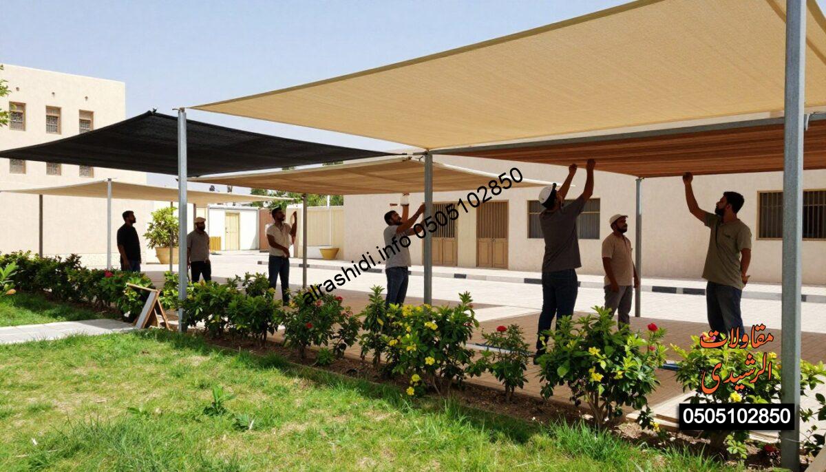 A realistic scene depicting workers in professional attire installing various types of shades in a sunny outdoor setting in southern Riyadh. In the foreground, focus on a team of skilled workers assembling a fabric shade structure over a garden area, showcasing a vibrant green lawn and blooming flowers. In the middle ground, include partially constructed shades made of metal and wood, emphasizing diverse designs suitable for parking areas and schools. In the background, capture elements of the local architecture typical of southern Riyadh, with clear blue skies above. Use bright, natural lighting to create a warm and inviting atmosphere, and shoot from a slightly elevated angle to provide a comprehensive view of the installation process.