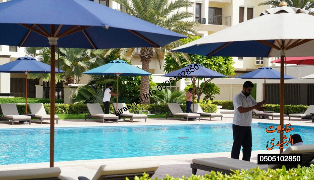 A serene poolside scene in East Riyadh featuring elegant pool umbrellas for shade, showcasing a blend of safety and luxury. In the foreground, an array of stylish umbrellas with vibrant colors offering protection from the sun are strategically positioned around a crystal-clear pool. In the middle ground, professional workers clad in modest, professional attire are installing the sturdy poles and fabric, demonstrating a commitment to quality and safety. The background reveals a beautiful residential setting with lush greenery and well-maintained gardens under bright, natural sunlight. The atmosphere is tranquil and inviting, perfect for relaxation. The overall composition balances focus on the workers and the luxurious atmosphere of the pool area, captured from a slightly elevated angle to emphasize depth and clarity. A serene poolside scene in East Riyadh featuring elegant pool umbrellas for shade, showcasing a blend of safety and luxury. In the foreground, an array of stylish umbrellas with vibrant colors offering protection from the sun are strategically positioned around a crystal-clear pool. In the middle ground, professional workers clad in modest, professional attire are installing the sturdy poles and fabric, demonstrating a commitment to quality and safety. The background reveals a beautiful residential setting with lush greenery and well-maintained gardens under bright, natural sunlight. The atmosphere is tranquil and inviting, perfect for relaxation. The overall composition balances focus on the workers and the luxurious atmosphere of the pool area, captured from a slightly elevated angle to emphasize depth and clarity.