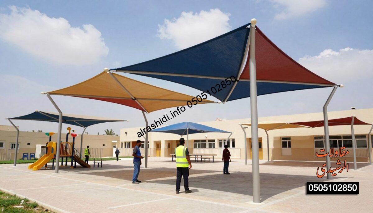 A vibrant schoolyard scene showcasing the installation of modern shade structures designed specifically for schools in West Riyadh. In the foreground, skilled workers in professional attire diligently set up large, colorful canopies, providing shade over playgrounds and outdoor study areas. The middle ground features various completed shades in different shapes and sizes, illustrating the functional and aesthetic aspects of the designs. The background reveals a clear blue sky with scattered clouds, emphasizing a bright and sunny day. Soft natural lighting enhances the colors of the structures and the surrounding environment, creating an inviting atmosphere. The angle captures both the installation process and the overall layout, highlighting the importance of quality and durability in school shade designs.